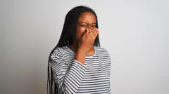 Young african american woman wearing striped t-shirt standing over isolated white background smelling something stinky and disgusting.