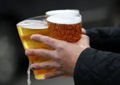Um homem segurando três pints com cerveja
