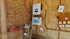 Sudut kafe Min. Dindingnya terbuat dari anyaman bambu, dengan dua unit daya terpasang dan terhubung ke kabel yang menggantung ke bawah hingga ke lantai.