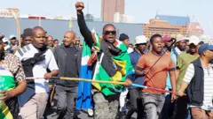 Man hold im hand up during protest, oda men dey im side