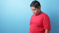 Anak laki-laki Asia berbadan gemuk melihat ke bawah.