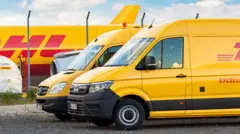 Dwa żółte samochody dostawcze DHL stoją przed samolotem transportowym zaparkowanym na terminalu lotniska Lipsk-Halle