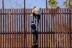 Migrantes intentan trepar la barrera fronteriza desde Mexicali, México hacia Calexico, EE. UU., el 13 de mayo de 2023 en Mexicali, Baja California. +Gary Coronado / Los Angeles Times vía Getty Images)