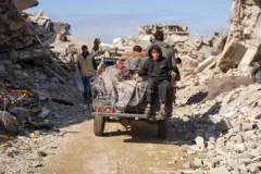 صورة تظهر الحياة اليومية في مخيم جباليا ، بقطاع غزة، حيث يجلس طفل على ظهر سيارة، وحوله مبانٍ مدمرة.