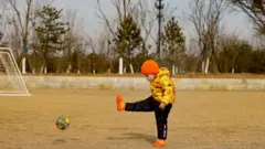 Criança chinesa chuta bola em campo