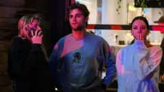 悉尼邦迪海灘外數名途人遠眺槍擊現場，一名女士（右）掩面神傷（14/12/2025）