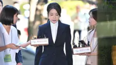 Kim Keon Hee entra no tribunal com a cabeça baixa, enquanto repórteres com microfones tentam falar com ela
