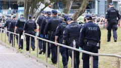 Группа полицейских в синей форме идет по газону вдоль мощеной плиткой дорожки