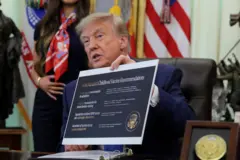 Trump, sentado diante de mesa e com olhar sério, segura cartaz com novas recomendações sobre vacinação infantil