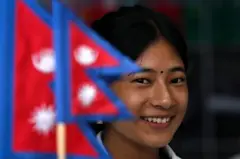 नेपालको राष्ट्रिय झण्डापछाडि हँसिलो मुद्रामा उभिएकी एक युवती