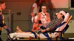 Uma mulher com uma bandagem na cabeça é transportada em uma maca.