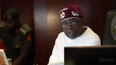 Aarẹ Tinubu pẹlu aṣọ funfun ati fila idanimọ rẹ