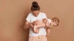 Mulher com bebê no colo, verificando seu cocô