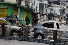 Miembros de la unidad especial de la policía militar patrullan una calle durante un operativo policial contra el narcotráfico. Están detrás de dos autos incendiados en la favela de Penha, en Río de Janeiro.