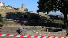 Taśma policyjna otacza na wpół zawaloną fontannę w mieście Ciudad Rodrigo. W tle drzewa i trawiaste wzgórze, za którym widać kamienną wieżę kościelną