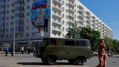 A vehicle drives past a mural dedicated to the upcoming anniversary of the taking control of the city by Russian armed forces in the course of Russia-Ukraine conflict, in Mariupol, a Russian-controlled city of Ukraine, May 18, 202