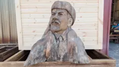 Ahşap Lenin büstü. Büstte Lenin şapkası, kabanı ve kravatıyla görülüyor. 