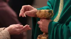 Close na mão de um padre entregando a óstia a uma pessoa