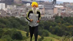 Fauja Singh koşu antremanı yapıyor, arkasında Edinburgh manzarası var.