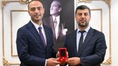 Eray Karadeniz ve yanında takım elbiseli bir kişi daha bir yüzüğü aralarında paylaşıyor.
