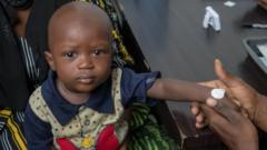 En Gambie, un jeune enfant se fait appliquer au poignet un patch de microréseau pour le vacciner contre la rougeole.
