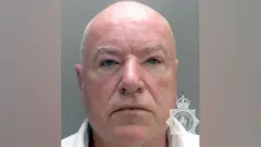 Neil Foden in a police custody photo, staring expressionlessly at the camera