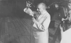 Dom Hélder Câmara sorrindo, acenando e falando ao microfone