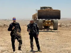 Dois policiais vigiando uma escavadeira que está ampliando o assentamento de Carmel perto de Umm al-Khair, no sul da Cisjordânia