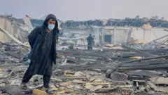 Человек в медицинской маске ходит по обломкам реабилитационного центра в Кабуле