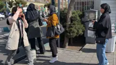 Несколько женщин на улице Тегерана, одна с поднесенной ко лбу рукой разговаривает по телефону