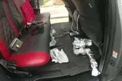 Imagens da câmera corporal da polícia mostram vários celulares nos bancos traseiros de um carro cinza, com embalagens de papel alumínio espalhadas pelo chão do carro.