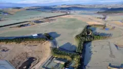 Uma foto aérea de uma área rural remota com colinas ao longe e uma vasta extensão de grama cercada por árvores em primeiro plano.