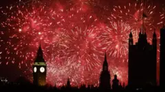 たくさんの打ち上げ花火で赤くなった夜空を背景に、時計の面が白く光る「ビッグベン」をはじめウェストミンスター宮殿（イギリス議会議事堂）の塔が黒いシルエットになっている
