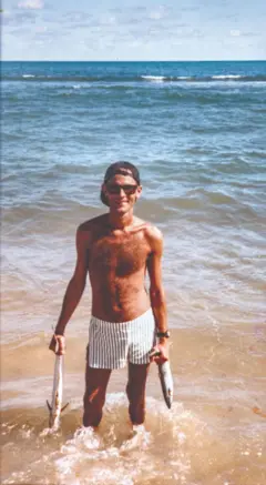 Cazuza sorrindo na beira do mar, segurando dois peixes, um em cada mão