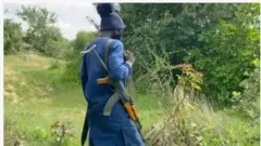 Aworan agbebọn ọkunrin ninu igbo, o de fila dudu, wọṣọ alawo aro