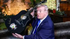 Donald Trump elinde bir gitarla poz veriyor ve bir şeyler anlatıyor.