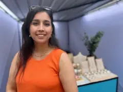 Mujer vestida de naranja frente a su negocio de joyas.