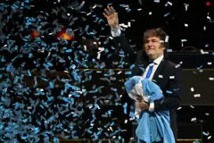 Milei saúda o público durante o lançamento de seu novo livro, segurando a bandeira argentina.