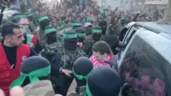 شبه‌نظامیان حماس در حال تحویل دورون اشتاینبرکر، یکی از گروگان‌های اسرائیلی آزاد شده در جریان مبادله روز دوم آتش‌بس غزه