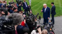 ホワイトハウスの庭で、カメラやマイクを構える大勢の記者団を前に、指さしながら話すスーツ姿のトランプ氏