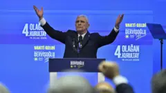 Müsavat Dervişoğlu mavi zemin üzerine partisinin amblemi ve 4. olağan genel kurultay yazısı ile kürsüde kollarını iki yana kaldırmış halde salonu selamlıyor