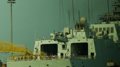 Guindaste abaixa um helicóptero sobre um navio militar atracado em Dalian, na China, sob os olhares da tripulação