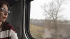 Uma mulher de óculos olha pela janela de um trem.