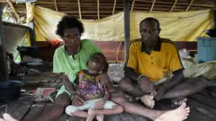 Keluarga Maurenus Merne tinggal di Kampung Anggreso, Kabupaten Mamberamo Raya. Anak bungsunya, Petra, lumpuh sejak balita dugaannya selama mengandung, mama Ester tidak mendapatkan asupan makanan bergizi dan vitamin yang memadai.