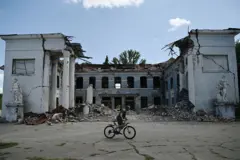 Um homem anda de bicicleta perto de um prédio destruído em Druzhkivka, região de Donetsk, em 15 de agosto de 2025, em meio à invasão russa na Ucrânia.