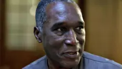 Dr Eugène Rwamucyo ubwo yari ageze mu rukiko rw'ibanze rw'i Paris mu Bufaransa, ku itariki ya mbere Ukwakira (10) mu 2024. Yambaye ishati y'ibara risa n'ivu idafite ikora, areba ku ruhande. Afite umusatsi mucye urimo imvi.