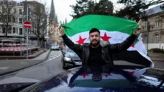 صورة تظهر رجلاً يحمل علم "الثورة السورية" يخرج من سيارة في ألمانيا محتفلاً بسقوط بشار الأسد.


