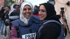 Mariam Dagga (kiri), jurnalis visual Palestina yang bekerja lepas untuk AP, memeluk seorang rekan jurnalis di Khan Yunis di Jalur Gaza selatan pada 18 Januari 2025.