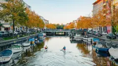 Imagem de canal de Copenhague, na Dinamarca, com barcos e pessoas andando de caiaque
