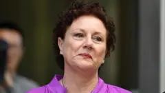Kathleen Folbigg dey wear purple shirt. She get short curly brown hair.